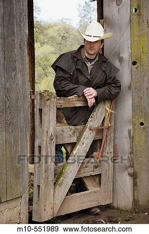 Cowboy up against gate and old rugged barn in the country on a ranch looking downward in a relaxed style. View Large Photo Image Stock Photo - Cowboy up against gate and old rugged barn in the country on a ranch looking downward in a relaxed style.. Fotosearch