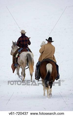 Stock Photo - Cowboys riding away through the snow, Shell, Wyoming. Usa.. Fotosearch