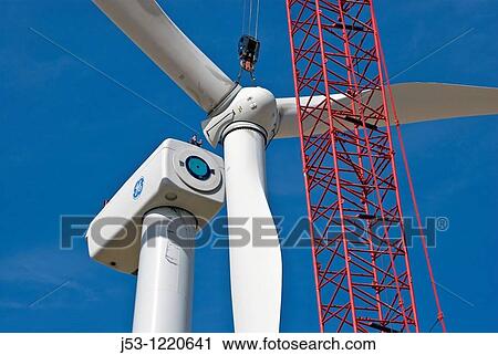 Stock Image - Crane lifting wind turbine rotor into position, note maintenance workers watching from top of nacelle. Fotosearch