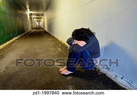 Stock Image - Crime scene concept photo of rape victim. A sad woman sits on the floor of a dark tunnel.. Fotosearch
