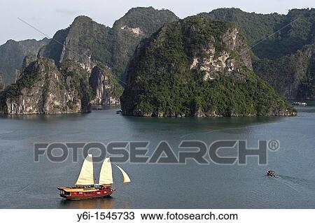 Stock Image - Cruising junk with sails hoisted Halong Bay Vietnam. Fotosearch