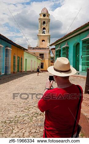 Cuba Trinidad tourist with hat shooting video of old cobblestone street and beautiful church in center of town. View Large Photo Image Picture - Cuba Trinidad tourist with hat shooting video of old cobblestone street and beautiful church in center of town.. Fotosearch