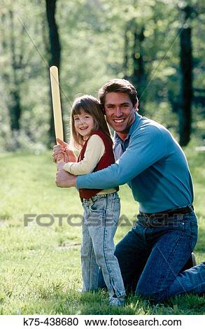 Stock Image - Dad teaching daughter how to hold a bat. Fotosearch