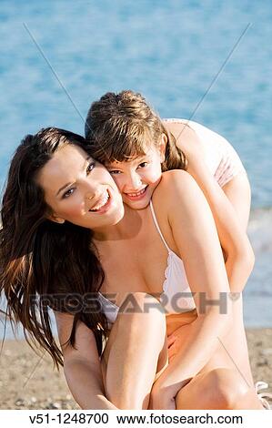 Stock Image - Daughter giving a hug to her mother in the seashore at the beach. Fotosearch