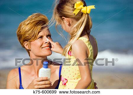Stock Photo - Daughter putting suntan lotion on mom's nose. Fotosearch