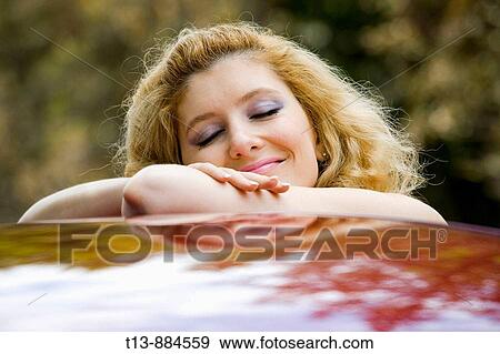 Stock Photo - Daydreaming young woman on top of a car. Fotosearch