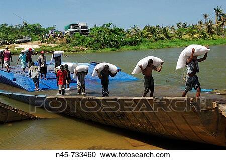 Stock Image - Destroyed bridge after a cyclone, local people carrying goods from one to the other side, Toamasina Province, Madagascar. Fotosearch