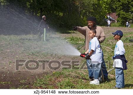 Detroit, Michigan - A man directs two boys using a fire hose to water part of the two-acre D-town Farm, an urban farm in a city park The farm is operated by the nonprofit Detroit Black Community Food Security Network View Large Photo Image Stock Photo - Detroit, Michigan - A man directs two boys using a fire hose to water part of the two-acre D-town Farm, an urban farm in a city park The farm is operated by the nonprofit Detroit Black Community Food Security Network. Fotosearch