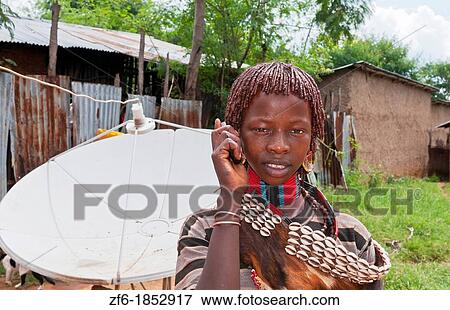 Dimeka Ethiopia Africa village Lower Omo Valley portrait of young Hamar girl with cell phone communicating and satellite dish in back 17 View Large Photo Image Stock Photo - Dimeka Ethiopia Africa village Lower Omo Valley portrait of young Hamar girl with cell phone communicating and satellite dish in back 17. Fotosearch