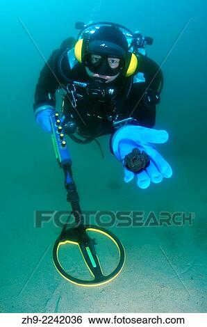 Stock Photograph - Diver with the metal detector displays the found ancient coins, lake Baikal, Siberia, Russia, Eurasia.. Fotosearch