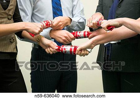 Stock Image - Diverse business team having fun pulling crackers at their office Christmas party. Fotosearch