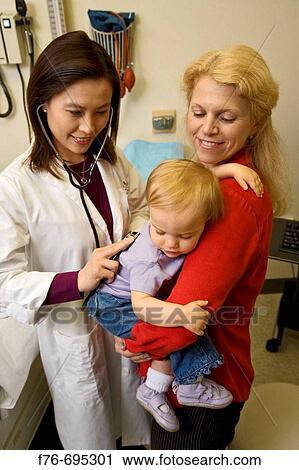 Doctor / pediatrician examines baby girl being held by her mother in medical office during physical exam View Large Photo Image Stock Image - Doctor / pediatrician examines baby girl being held by her mother in medical office during physical exam. Fotosearch