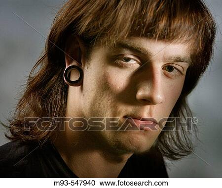 Dramatically lit close-up portrait of long-haired young caucasian man with loop holding open large piercing of earlobe. Surly expression. View Large Photo Image Stock Image - Dramatically lit close-up portrait of long-haired young caucasian man with loop holding open large piercing of earlobe. Surly expression.. Fotosearch