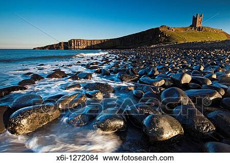 Picture - Dunstanburgh Castle, with basalt boulders on beach, autumn, Northumberland, England. Fotosearch