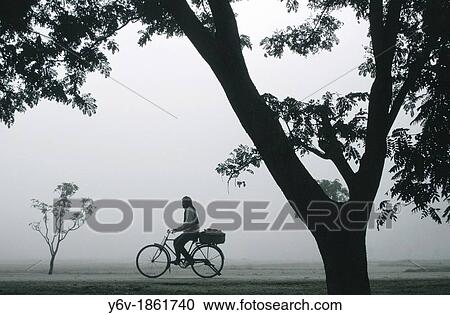 Stock Image - During a foggy morning, a man is riding a cycle. Tera? region, Nepal.. Fotosearch