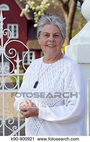 Elderly caucasian woman standing at a white metal gate with a traditional northfrisian house in the background during sunny weather, smiling and looking into the camera, Island of Amrum, Northfrisian, Schleswig_Holstein, Northern Germany, Europe View Large Photo Image Stock Image - Elderly caucasian woman standing at a white metal gate with a traditional northfrisian house in the background during sunny weather, smiling and looking into the camera, Island of Amrum, Northfrisian, Schleswig_Holstein, Northern Germany, Europe. Fotosearch