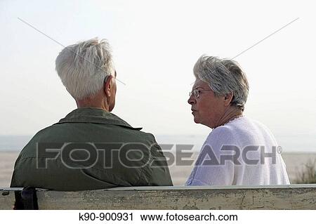 Elderly couple sitting on a bench, seen from backside, talking to each other and the senior man carrying a hearing aid, Island of Amrum, Northfrisian, Schleswig_Holstein, Northern Germany, Europe View Large Photo Image Stock Image - Elderly couple sitting on a bench, seen from backside, talking to each other and the senior man carrying a hearing aid, Island of Amrum, Northfrisian, Schleswig_Holstein, Northern Germany, Europe. Fotosearch