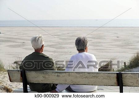 Elderly couple sitting on a bench, seen from backside, looking over the wide beach with the sea in the background, Island of Amrum, Northfrisian, Schleswig_Holstein, Northern Germany, Europe View Large Photo Image Stock Photo - Elderly couple sitting on a bench, seen from backside, looking over the wide beach with the sea in the background, Island of Amrum, Northfrisian, Schleswig_Holstein, Northern Germany, Europe. Fotosearch