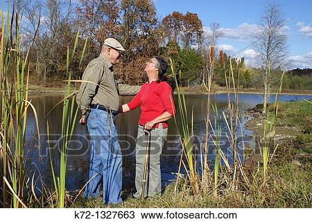 Elderly couple stand talking by a lake in the fall View Large Photo Image Stock Image - Elderly couple stand talking by a lake in the fall. Fotosearch