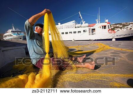 Stock Image - Elderly greek fisherman repairing fishnets at the old harbour, Mykonos, Cyclades Islands, Greek Islands, Greece, Europe.. Fotosearch