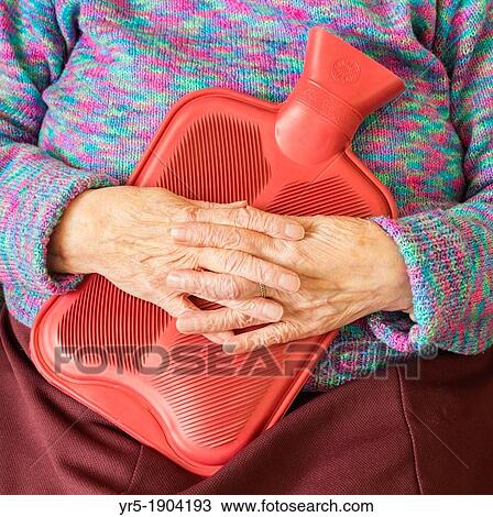 Stock Image - Elderly lady kkeping warm in winter with hot water bottle England, United Kingdom. Fotosearch