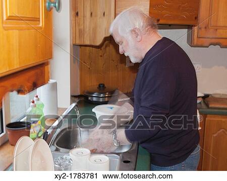 Stock Image - Elderly man at sink washing dishes. Fotosearch
