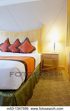 Stock Photography - elegant bed setting with silk pillows and bed runner Scene illuminated by a lamp. Fotosearch