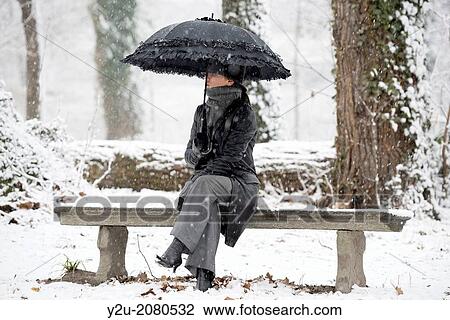 Elegant woman sitting on a bench with umbrella when it's snowing in locarno ticino switzerland. View Large Photo Image Stock Image - Elegant woman sitting on a bench with umbrella when it's snowing in locarno ticino switzerland.. Fotosearch