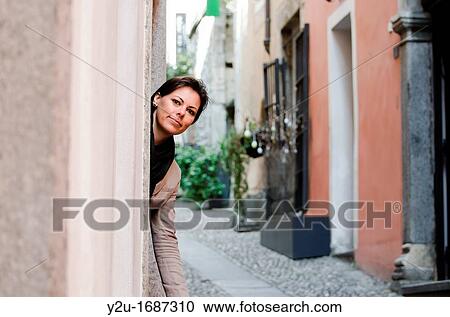 Stock Image - Elegant woman watching out from a door in an alley. Fotosearch