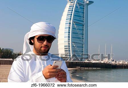 Emirate arab man with cell phone texting in front of Worlds only 7 star hotel in Dubai UAE called the Burj Al Arab with luxury and water at beach in United Arab Emirates. View Large Photo Image Stock Image - Emirate arab man with cell phone texting in front of Worlds only 7 star hotel in Dubai UAE called the Burj Al Arab with luxury and water at beach in United Arab Emirates.. Fotosearch