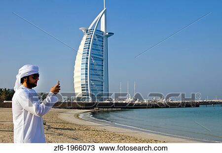 Emirate arab man with cell phone texting in front of Worlds only 7 star hotel in Dubai UAE called the Burj Al Arab with luxury and water at beach in United Arab Emirates. View Large Photo Image Stock Image - Emirate arab man with cell phone texting in front of Worlds only 7 star hotel in Dubai UAE called the Burj Al Arab with luxury and water at beach in United Arab Emirates.. Fotosearch