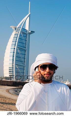 Emirate arab man with cell phone talking in front of Worlds only 7 star hotel in Dubai UAE called the Burj Al Arab with luxury and water at beach in United Arab Emirates. View Large Photo Image Stock Photo - Emirate arab man with cell phone talking in front of Worlds only 7 star hotel in Dubai UAE called the Burj Al Arab with luxury and water at beach in United Arab Emirates.. Fotosearch