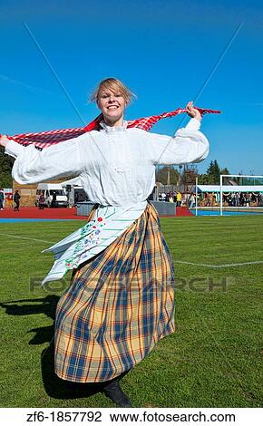 Stock Image - Energy of teenager girl spinning dance traditional dress portrait in costume with scarf at festival village near Vilnius Lithuania Lithuanian smile joyful joy. Fotosearch