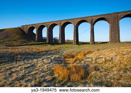 Stock Photography - England, North Yorkshire, Yorkshire Dales National Park. Ribblehead Viaduct, a railway viaduct across the valley of the River Ribble at Ribblehead in the Yorkshire Dales, with the peak of Whernside in the distance viewed on a frosty, spring morning.. Fotosearch