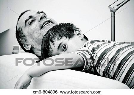 Escena familiar de padre e hijo descansando en el sofB View Large Photo Image Stock Photograph - Escena familiar de padre e hijo descansando en el sofB. Fotosearch