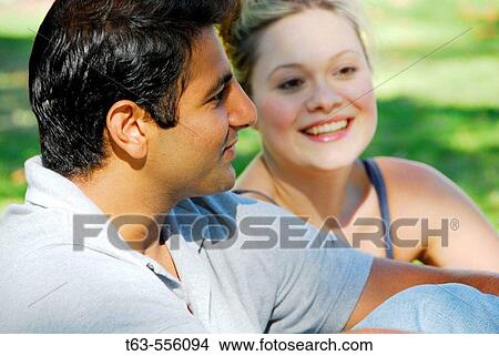 ethnic male and caucasion female sitting together outdoors View Large Photo Image Picture - ethnic male and caucasion female sitting together outdoors. Fotosearch