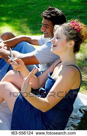 ethnic male and caucasion female sitting together outdoors- female dialing cellphone View Large Photo Image Picture - ethnic male and caucasion female sitting together outdoors- female dialing cellphone. Fotosearch