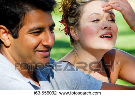 Stock Image - ethnic male and caucasion female sitting together outdoors. Fotosearch