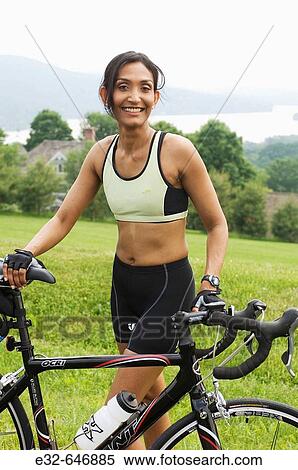 Stock Photography - Ethnic woman in exercise clothing with bicycle in scenic setting. Fotosearch