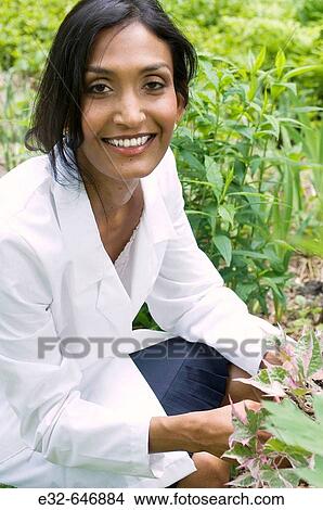 Ethnic woman in white lab coat holding plant in garden View Large Photo Image Picture - Ethnic woman in white lab coat holding plant in garden. Fotosearch