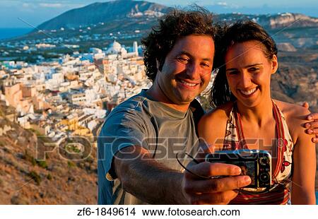Picture - European tourists taking picture of themselves overlooking Fira at sunset in Santorini Greece in the Greek Islands. Fotosearch