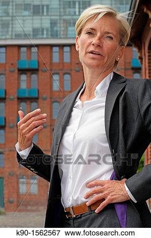 Executive woman, serious talking with open gesture, one hand at her hips, office building made of red brinks, with windows and balconies in the background, Hamburg, Germany, Europe View Large Photo Image Stock Photo - Executive woman, serious talking with open gesture, one hand at her hips, office building made of red brinks, with windows and balconies in the background, Hamburg, Germany, Europe. Fotosearch