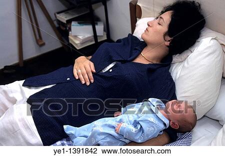 Stock Image - Exhausted woman sleeping with her five day old baby in her arms. Fotosearch
