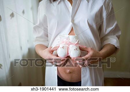 Stock Image - Expectant mother holding pink booties on belly. Fotosearch