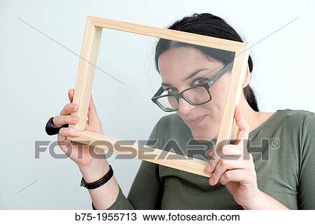 Face of young woman with glasses looking through a wooden frame View Large Photo Image Stock Image - Face of young woman with glasses looking through a wooden frame. Fotosearch