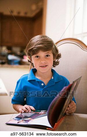 Fair haired young boy with a blue shirt opening a childrens book. View Large Photo Image Picture - Fair haired young boy with a blue shirt opening a childrens book.. Fotosearch