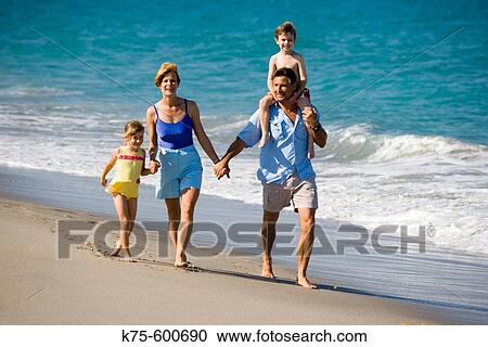 Stock Image - Family of 4 walking on beach. Fotosearch