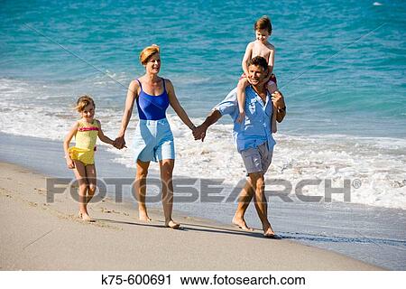 Stock Image - Family of 4 walking on beach. Fotosearch