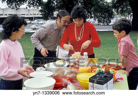 Family of four in the park with father supervising the serving of spaghetti at the picnic table View Large Photo Image Stock Photograph - Family of four in the park with father supervising the serving of spaghetti at the picnic table. Fotosearch