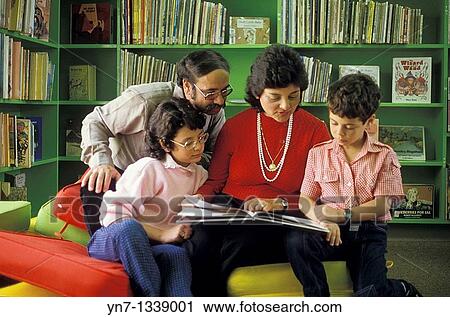 Stock Image - family of four reading together in the local library. Fotosearch